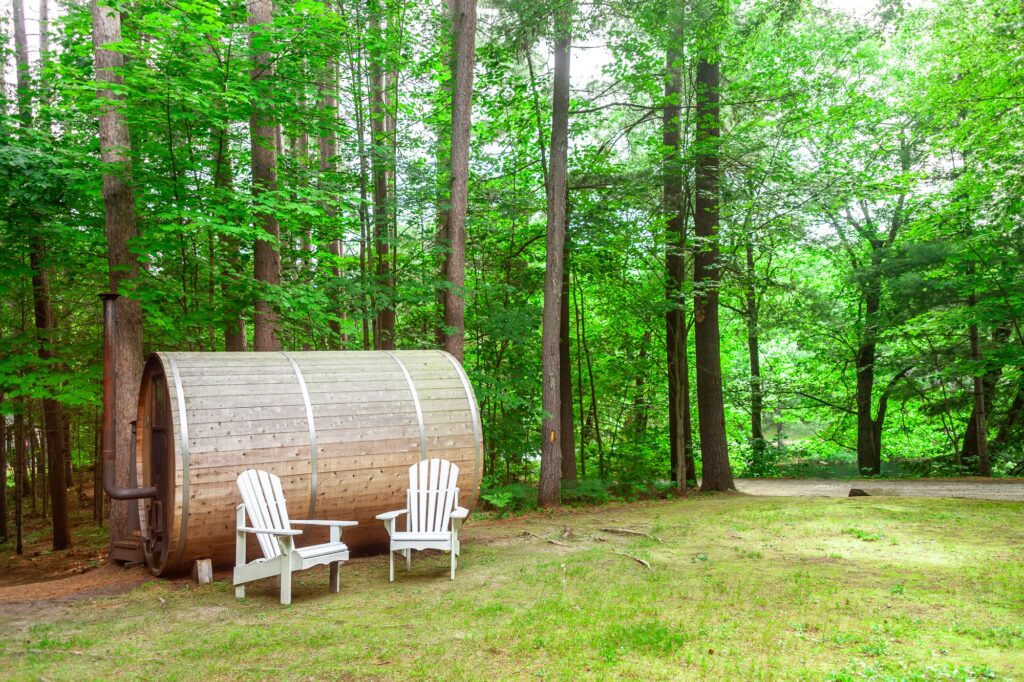 Wooden barrel sauna in lush forest with white Adirondack chairs at Trillium Resort and Spa Muskoka Huntsville Port Sydney