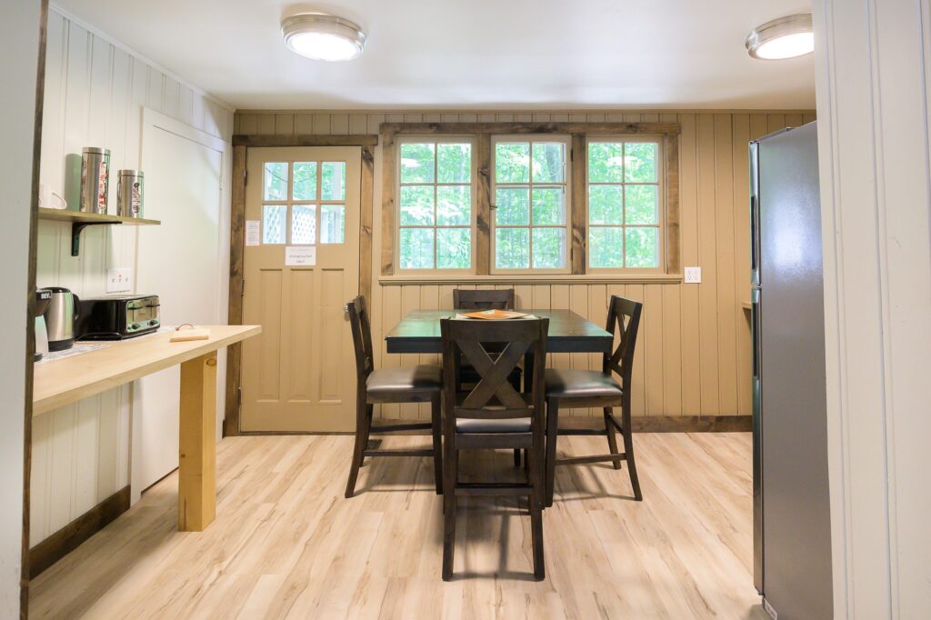Bright dining area and kitchenette with forest views through large windows in Falling Water private cottage at Trillium Resort Muskoka