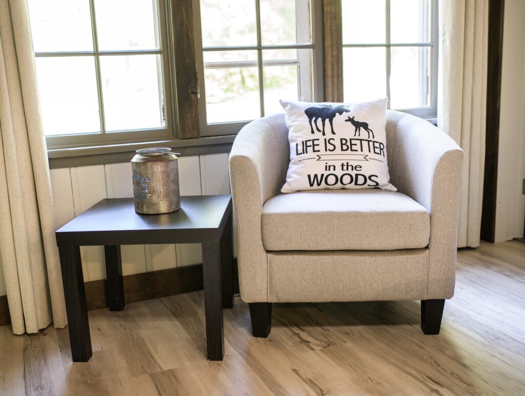 Sunlit sitting area with armchair overlooking forest through large windows in Rushing Water cottage at Trillium Resort and Spa Muskoka