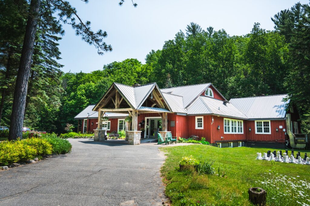 Trillium Resort and Spa red main lodge with post-and-beam design surrounded by lush summer greenery Muskoka Huntsville Port Sydney