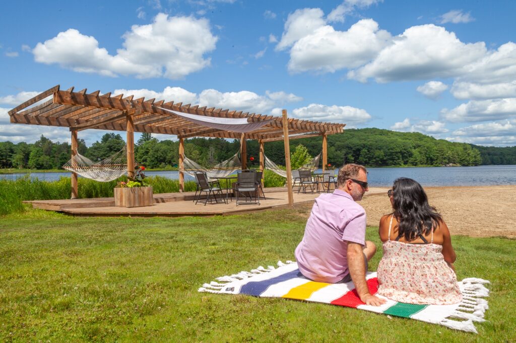Couple relaxing lakeside with pergola and Muskoka Adirondack chairs overlooking semi-private lake at Trillium Resort and Spa Port Sydney Huntsville